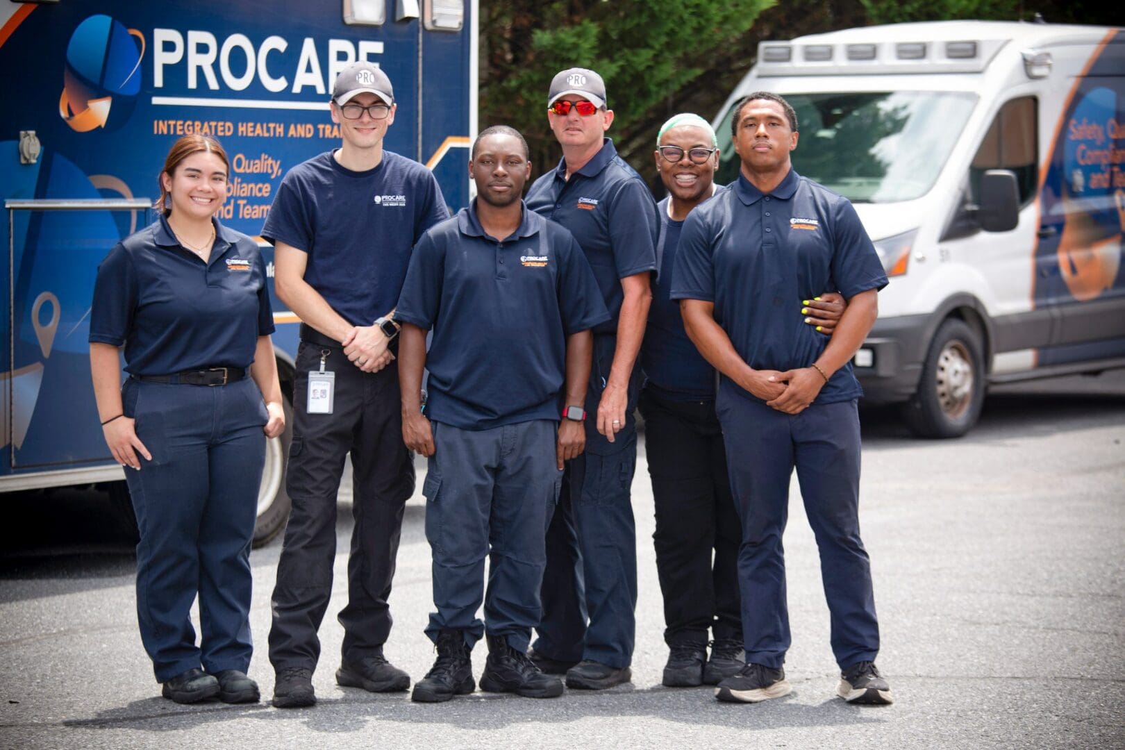 Six uniformed responders posing beside branded ambulances